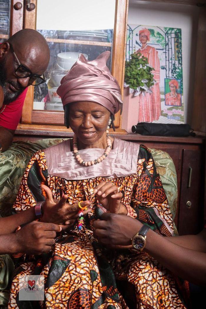 An older woman makes a friendship bracelet from colourful hair ties with visiting volunteers.